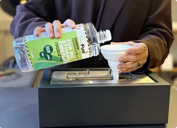 verser du combustible bioéthanol dans un brûleur à l’aide d’un entonnoir en plastique