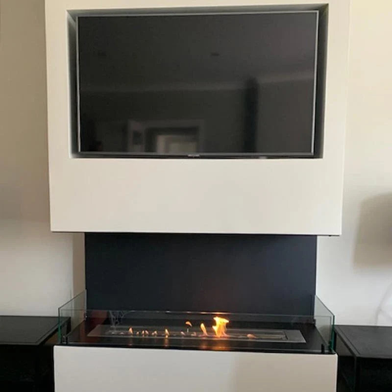 Foco Three 1200 built into a protruding wall pillar beneath a mounted TV, with a realistic lit ethanol flame, in a real customer's living room.